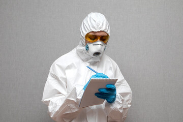 Women doctor wearing protective suit writes data about coronavirus during pandemic covid-2019. Protective suit, googles, gloves, respirator.\