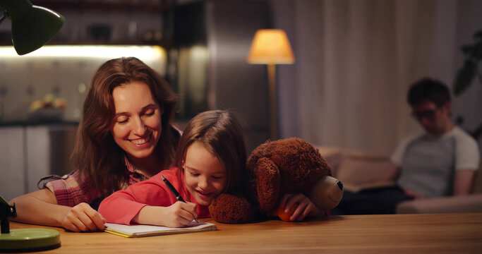 Mother and little daughter doing homework together in evening at home