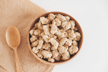 Raw dehydrated soy meat or dry soya chunks in wooden plate with a wooden spoon on white background. Top view. Copy, empty space for text
