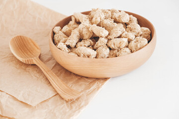 Raw dehydrated soy meat or dry soya chunks in wooden plate with a wooden spoon on white background. Top view. Copy, empty space for text
