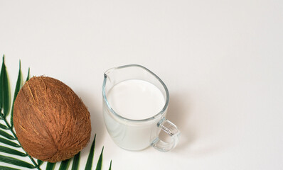 Summer background with palm leaf, coconut and vegan organic coconut milk in glass jug. Healthy eating concept. Minimal banner with copy space.