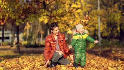 Naklejka premium Mom and son throw autumn leaves in autumn park, family fun. family enjoying a walk in nature. happy motherhood concept.