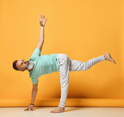 Mature handsome grey-haired brutal man wearing trendy sportswear practicing yoga in Ardha Chandrasana pose. Balance, harmony, strength and stretching. Studio shot on yellow background. Side view