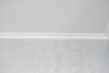 White ceiling with a white plinth in a room with gray painted walls. Decoration of the corner between the ceiling and the wall in the room. Ceiling molding in the interior. Detail of corner.