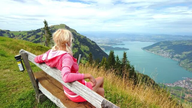 tourist woman sitting on a bench after trekking looking alpine panorama from Rigi Scheidegg to Krabel. Lake Lucerne, Lake Lauerz and Lake Zug. Tourism in Canton of Lucerne, Switzerland.