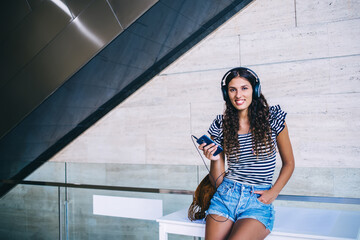 Cheerful woman listening to music with smartphone and headphones in building