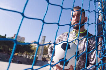 sportsman through goal net with a football ball