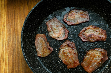 Closseup of fried fat bacon on the black pan on the wooden desk