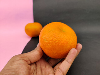 Man hand holding one tasty orange fruit isolated on pink and black background.