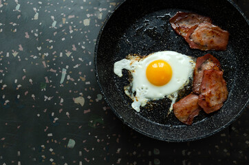 Top view of pan and fried egg, pieces of meat on it.Traditional fried bacon and egg