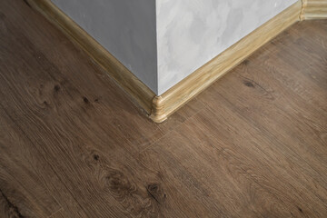 Laminate with plastic baseboard with a wooden texture. Newly installed wooden laminate flooring and baseboards in home. Modern design. Close up of plastic plinths on dark wooden oak floor parquet.