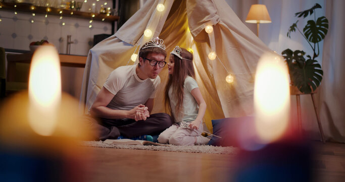 Father and daughter wearing crowns playing in toy wigwam at home - Powered by Adobe