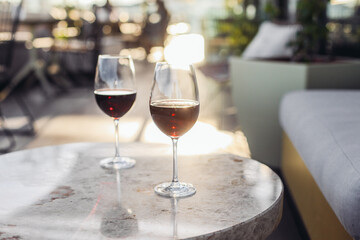 Two glasses of red wine on a sunny fancy restaurant terrace. Marble tables, cosy couch, sunset light, rooftop 