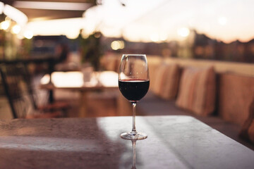 A glass of red wine on a restaurant terrace. Marble tables, lounge couches, pillows, evening light,...