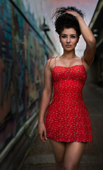 Fototapeta premium A beautiful young curly-hair woman in a little red dress is walking on the street. - Portrait Photography. 
