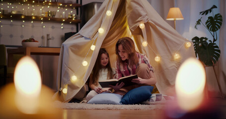 Mother and daughter are sitting in teepee tent reading stories © TommyStockProject