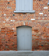 Very old brick wall with grey wooden door and grey shutters