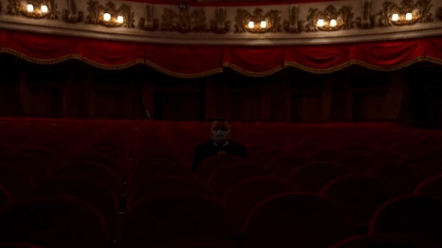 Man stands up from a red theater chair and throws medical mask away. Visitor in empty hall. Stop pandemic concept.