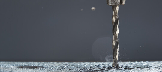 Obraz na płótnie Canvas Metal wet drill bit make holes in metal billet on industrial drilling machine with shavings on gray background.