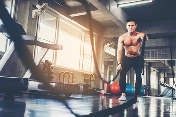 Fototapeta na wymiar Portrait of Athletic adult man with battle rope doing exercise in the fitness gym. Sports concept.