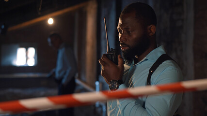 Fototapeta na wymiar African policeman in talking on radio set at crime scene