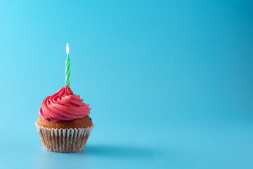 Pink birthday cupcake with green candle on blue background
