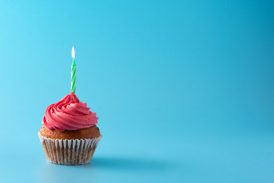 Pink birthday cupcake with green candle on blue background