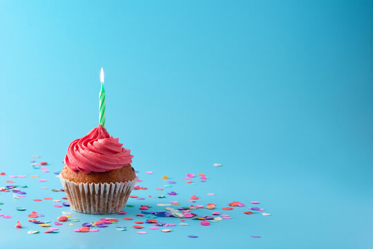 Pink birthday cupcake with green candle and confetti on blue background