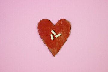 Cardboard heart on a pink background. White capsules on a red heart. Heart treatment. Red heart. Health concept