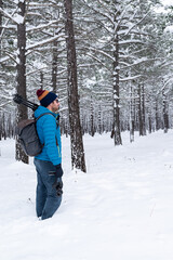 Side view of a male photographer standing in a snowy pine forest. 