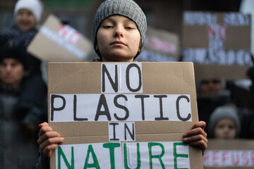 Young girl holding sign and demonstrating against plastic pollution with other activists