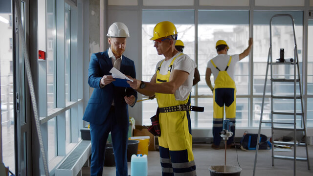 Contractor talking with builder in uniform and hardhat discussing office renovation plan
