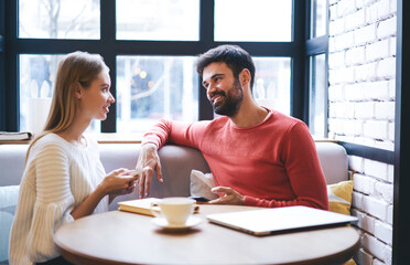 Positive couple communicating while sitting in cozy cafe with smartphones