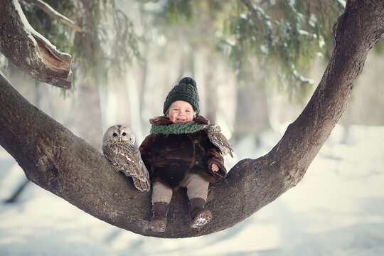 Little cute boy with owl sitting on the curved tree. Image with selective focus and toning.