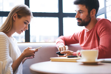 Fototapeta na wymiar Focused woman messaging on smartphone while sitting at cafe with boyfriend