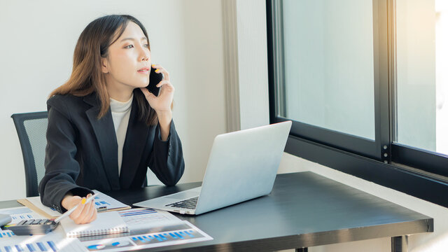 Young Asian businesswoman working at home on a black table with graph and calculator, notebook. - Powered by Adobe