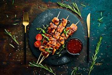 Chicken skewers with teriyaki sauce on a black stone plate. Rustic style. Barbecue menu.