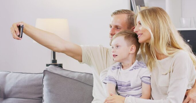 Smiling young family with little preschooler boy sit on couch in living room make self-portrait picture on cell together, happy parents with small child son have fun take selfie on smartphone at home.