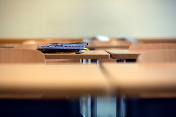 A copy, spiral noted pad and textbook on a school desk in a deserted classroom