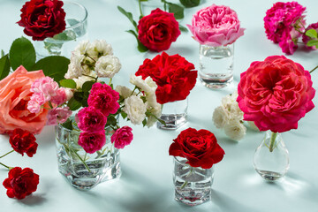 Multicolored rose flowers in glass vases on a blue background.