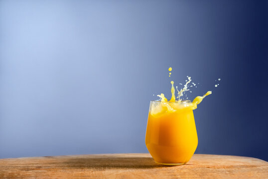 Glass of fresh orange juice splash on on wooden table and blue background. Dynamic pour of fruit juice in the morning. Space for text