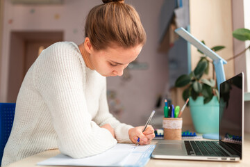 Fototapeta premium Beautiful schoolgirl studying at home doing school homework. Distance learning online education