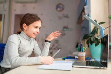 Cute little schoolgirl studying at home doing school homework. Distance learning online education