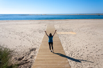 Young woman with arms outstretched walking down the beach walkway
