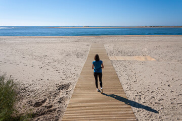 Young woman with arms outstretched walking down the beach walkway