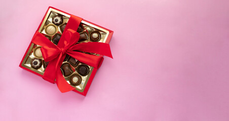 Box of chocolate pralines with red bow on pink background. Image with copy space