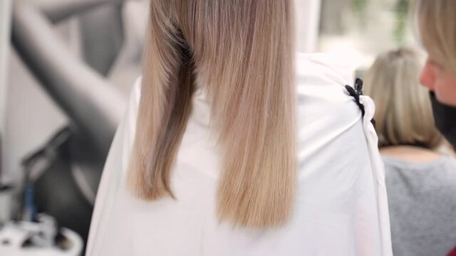a hairdresser with a protective mask in a beauty salon cuts blonde long hair, thrown forward over the client's face