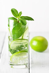 Mojito cocktail in a glass with mint, lime and ice on a white rustic table. Refreshing drink. Selective focus.