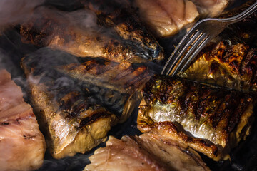 Grilled mackerel fish with smoke on a charcoal barbecue grill.