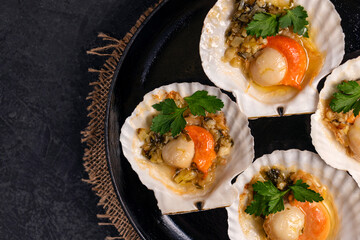 Scallops, lemon, garlic, parsley, butter and salt on black background. Close up baked scallops with caviar and creamy garlic sauce. Recipe for cooking scallops with caviar. Top view. Copy space.